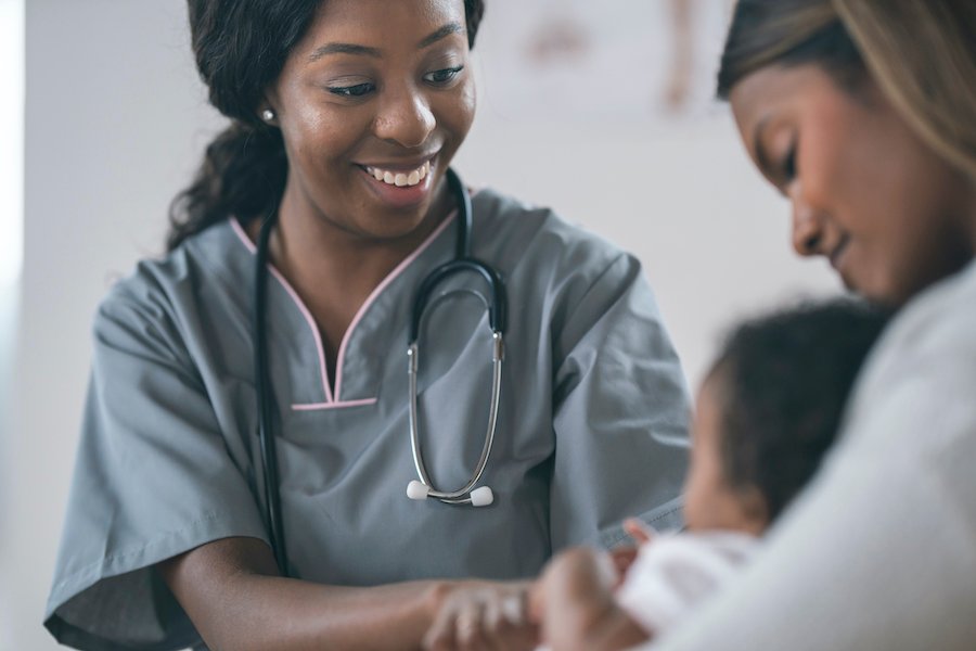 Black female physician smiling at Black newborn baby in his mom039s lap